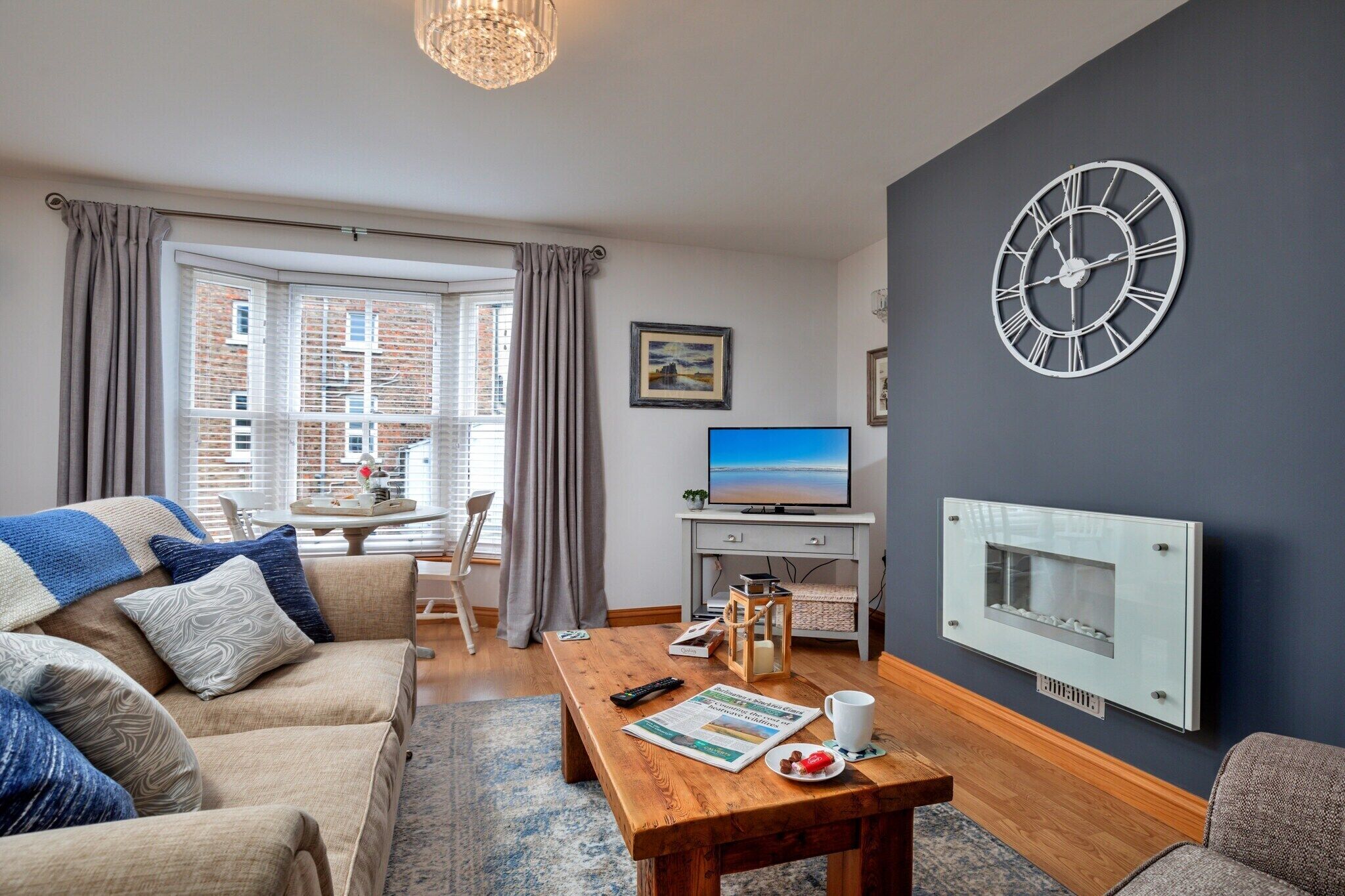 A modern living room with a sofa, a wooden coffee table, a television, and a large wall clock.