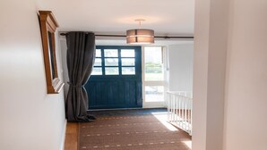 Um corredor com uma porta azul escura, um tapete estampado e um lustre.