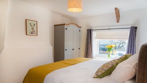 Quarto com cama, guarda-roupa, janela com cortinas e um quadro na parede.