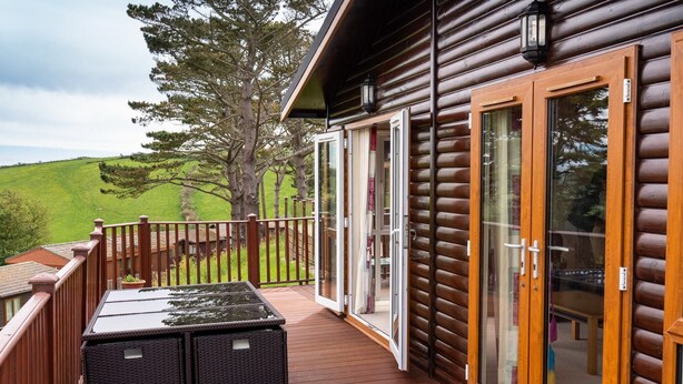 Um deck de madeira com uma porta de vidro que dá para um quarto, uma mesa e duas cestas de vime.
