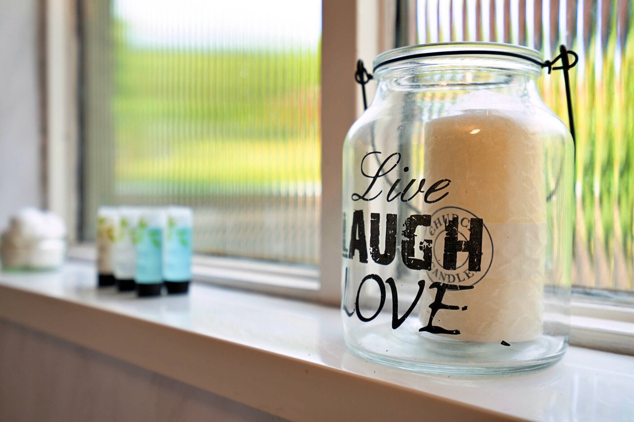 Una candela in un barattolo di vetro con l'incisione “Live LAUGH LOVE” su un davanzale.