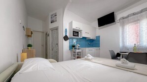 A hotel room with a bed, a desk, a TV, and a kitchenette.
