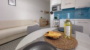 A modern living room with a sofa, a dining table with a placemat, a bottle of wine, and a kitchen area with cabinets and a microwave.