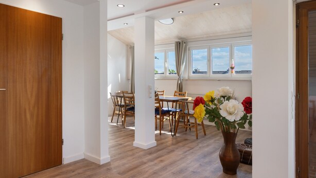 A spacious room with a wooden door, a dining area with wooden chairs and a table, and a large window with curtains. - Holiday Apartment 'Hannelore' with Shared Garden, Balcony and Wi-Fi (Radolfzell am Bodensee)