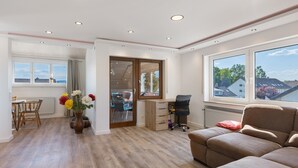 A modern living room with a sofa, a dining area with a table and chairs, a large window with a view, and a wooden floor. - Holiday Apartment 'Hannelore' with Shared Garden, Balcony and Wi-Fi (Radolfzell am Bodensee)