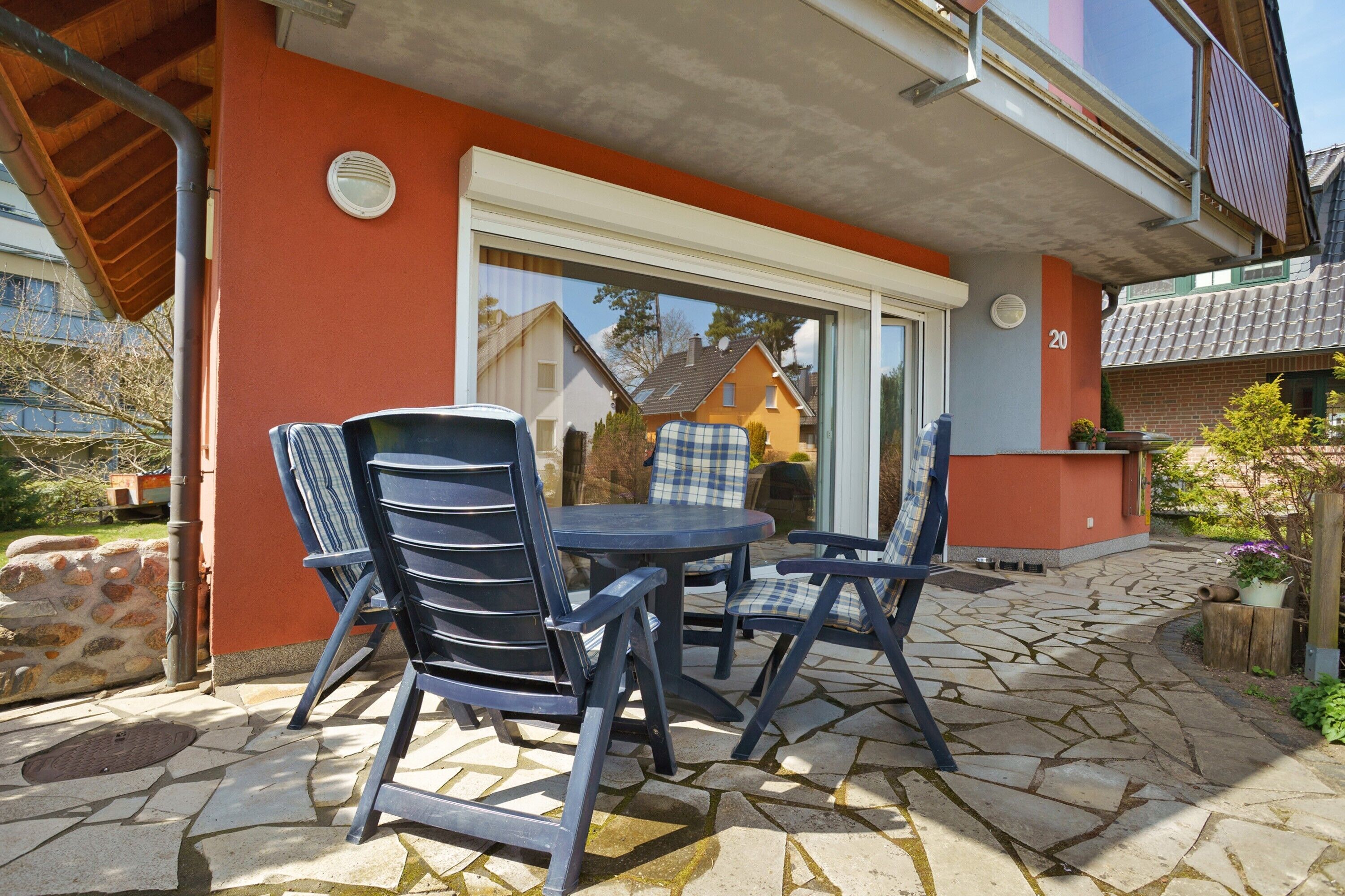 Une terrasse avec une table et des chaises, un sol en pierre et un mur rouge.