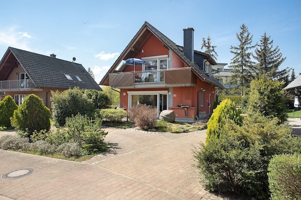 A two-story house with a balcony, a paved driveway, and surrounding greenery.