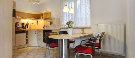 A compact kitchen with a dining table, chairs, and a window with curtains.
