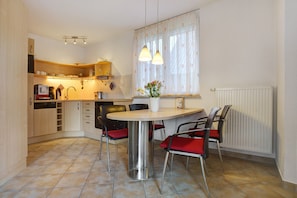 A compact kitchen with a dining table, chairs, and a window with curtains.