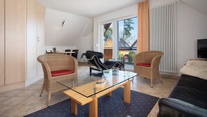 En moderne stue med et glasbord, fletstole, en sort lædersofa og udsigt ud