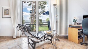Huoneessa on nojatuoli, pieni pöytä, työpöytä tietokoneella sekä lasioven kautta avautuva näkymä ulos.