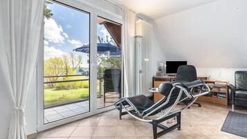 Une pièce avec une porte-fenêtre coulissante donnant sur un balcon, un fauteuil inclinable, un bureau avec un ordinateur et une bibliothèque.