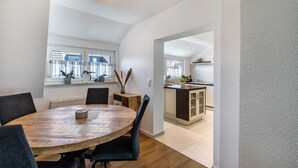 A modern kitchen with a wooden dining table and chairs, a built-in island, and a view through the window. - Apartment 'New Look' with Mountain View, Balcony and Wi-Fi (Geisenheim)