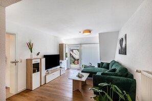 Un soggiorno moderno con televisione a schermo piatto, un divano verde, un tavolino da caffè e vista su un edificio.