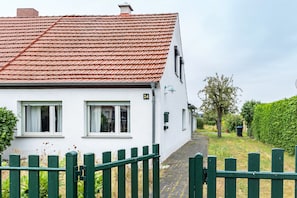 A white house with a red-tiled roof, a green gate, and a number '24' on the wall.