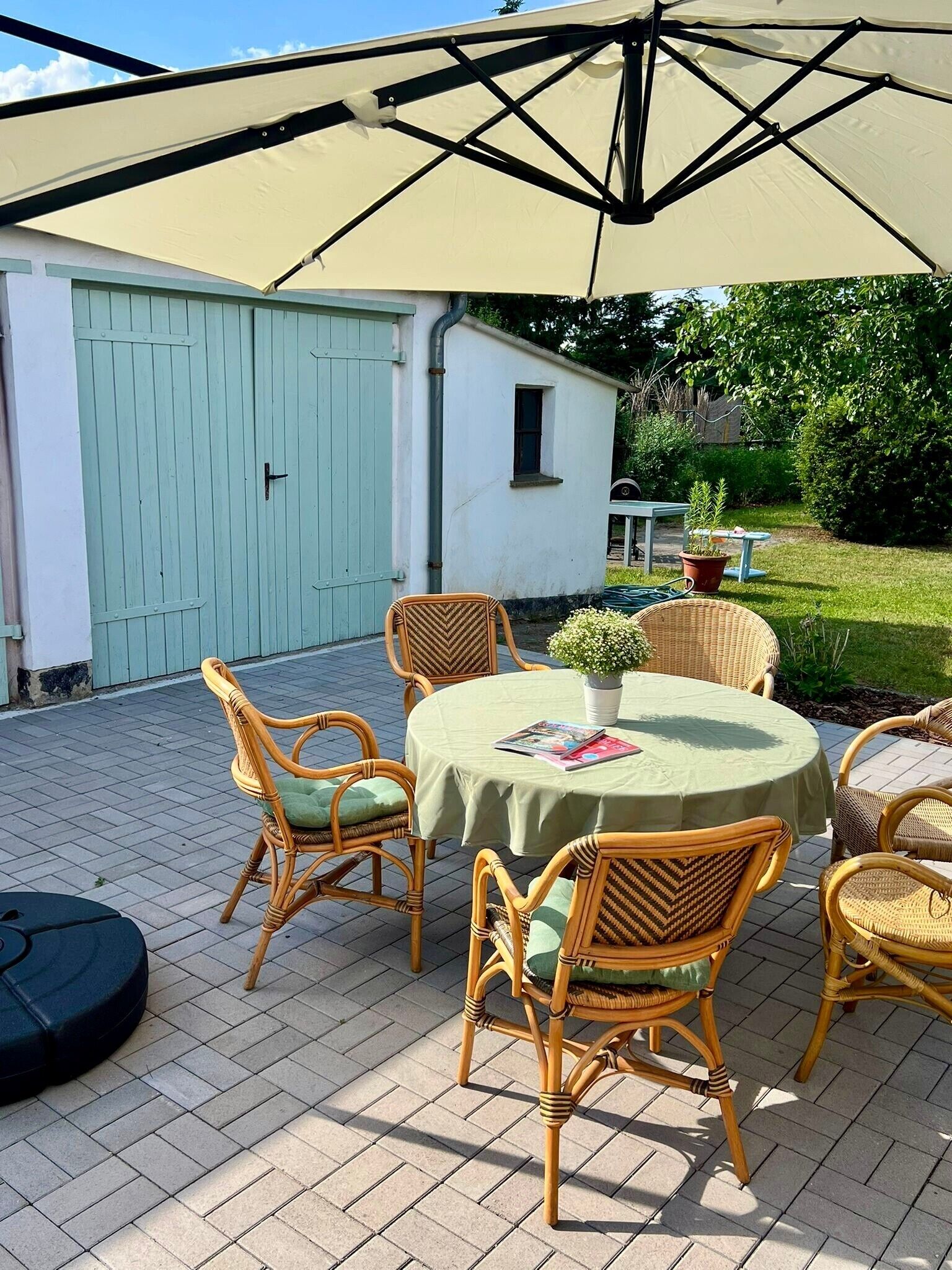 A patio with wicker furniture, a table with a green tablecloth, and a large umbrella.