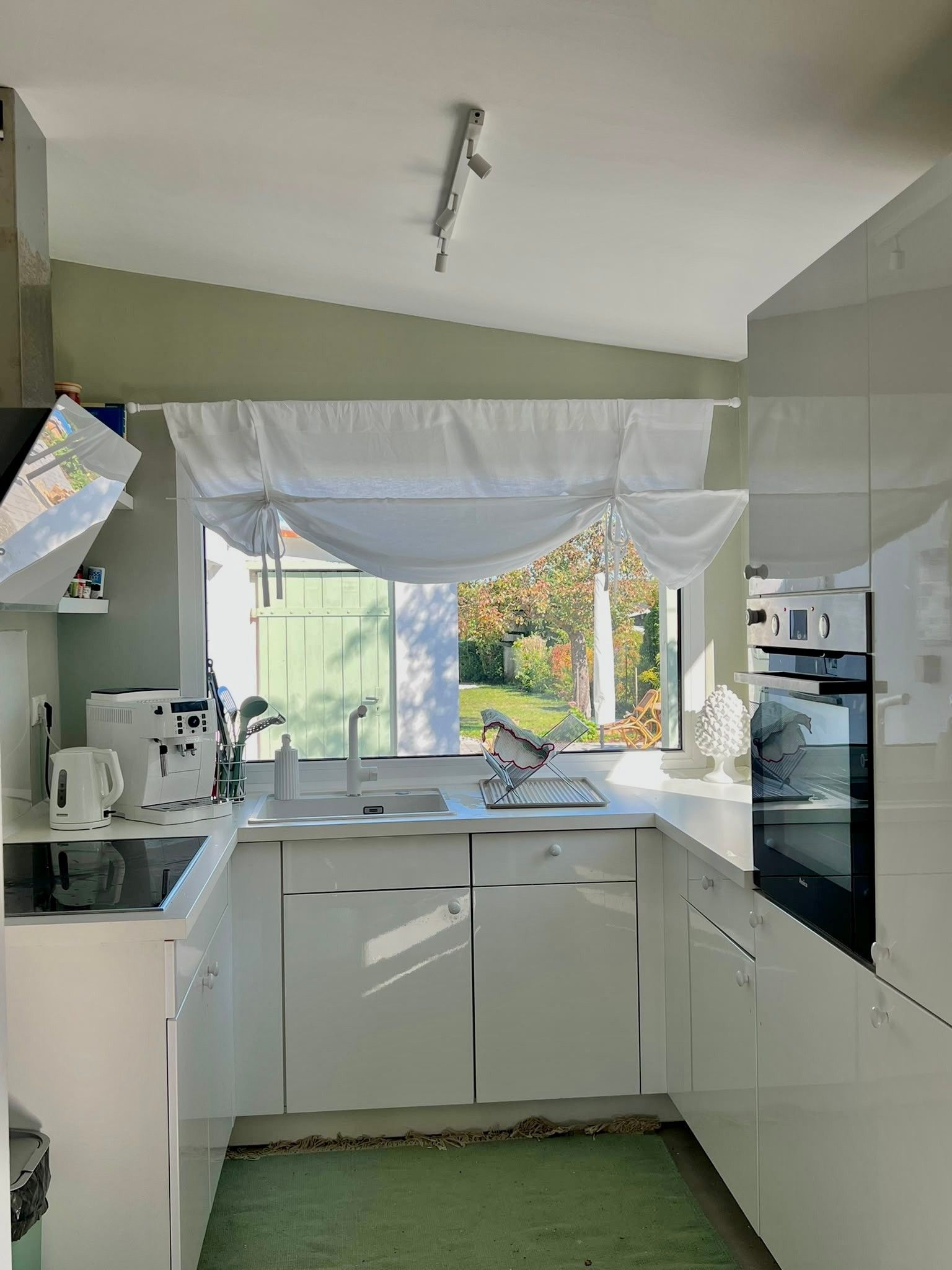 Une cuisine moderne avec des armoires blanches, un four encastré et une fenêtre donnant sur un jardin.