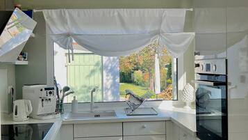 Une cuisine moderne avec des armoires blanches, un four encastré et une fenêtre donnant sur un jardin.