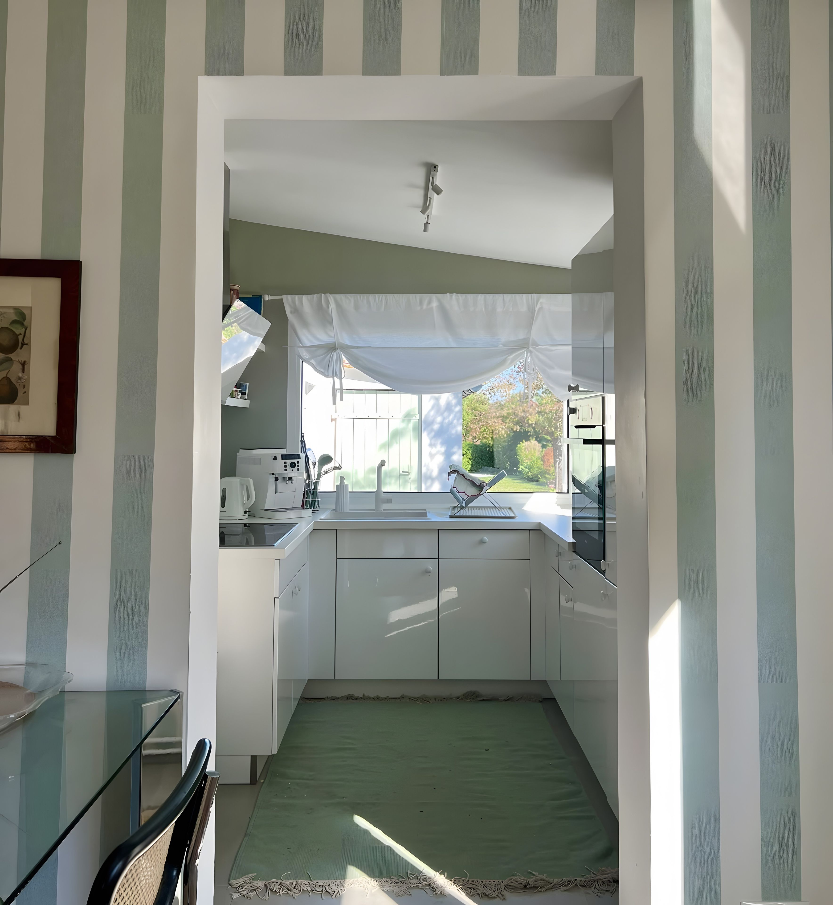 A narrow kitchen with a window, a sink, and a green mat.