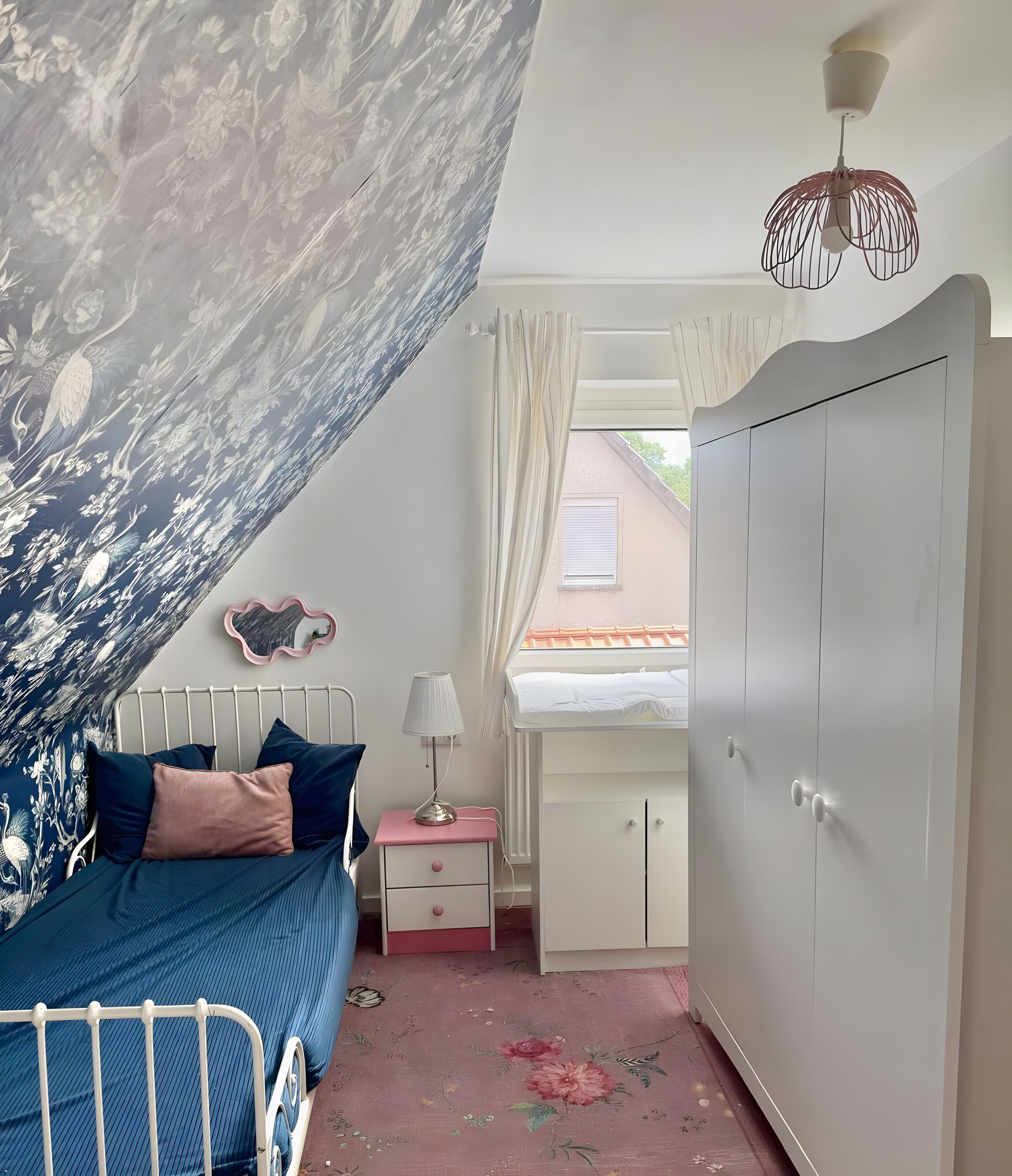 A bedroom with a bed, bedside table, lamp, wardrobe, and a window with curtains.