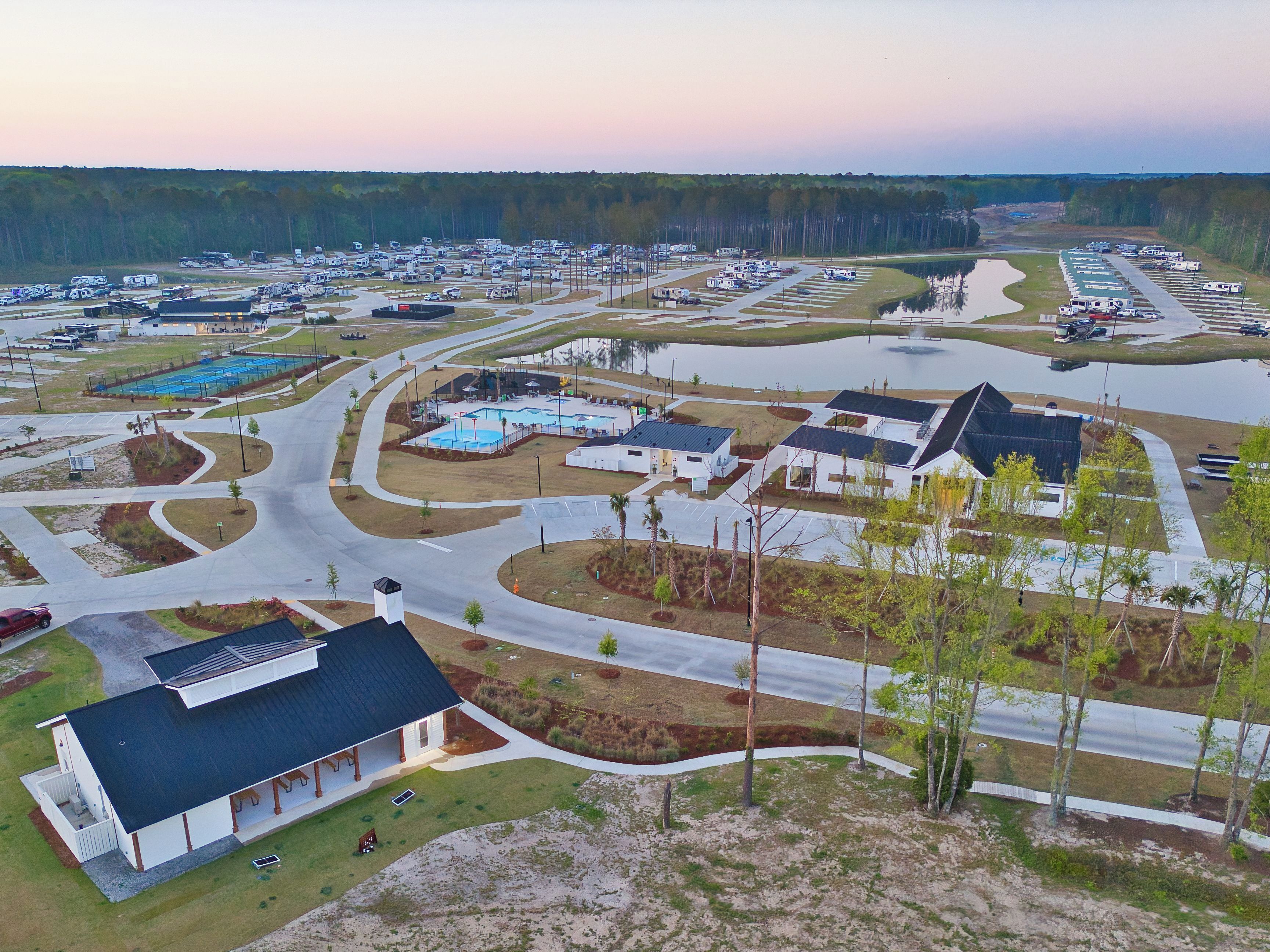 A large RV park with multiple parking areas, a swimming pool, and a building with a sloped roof.