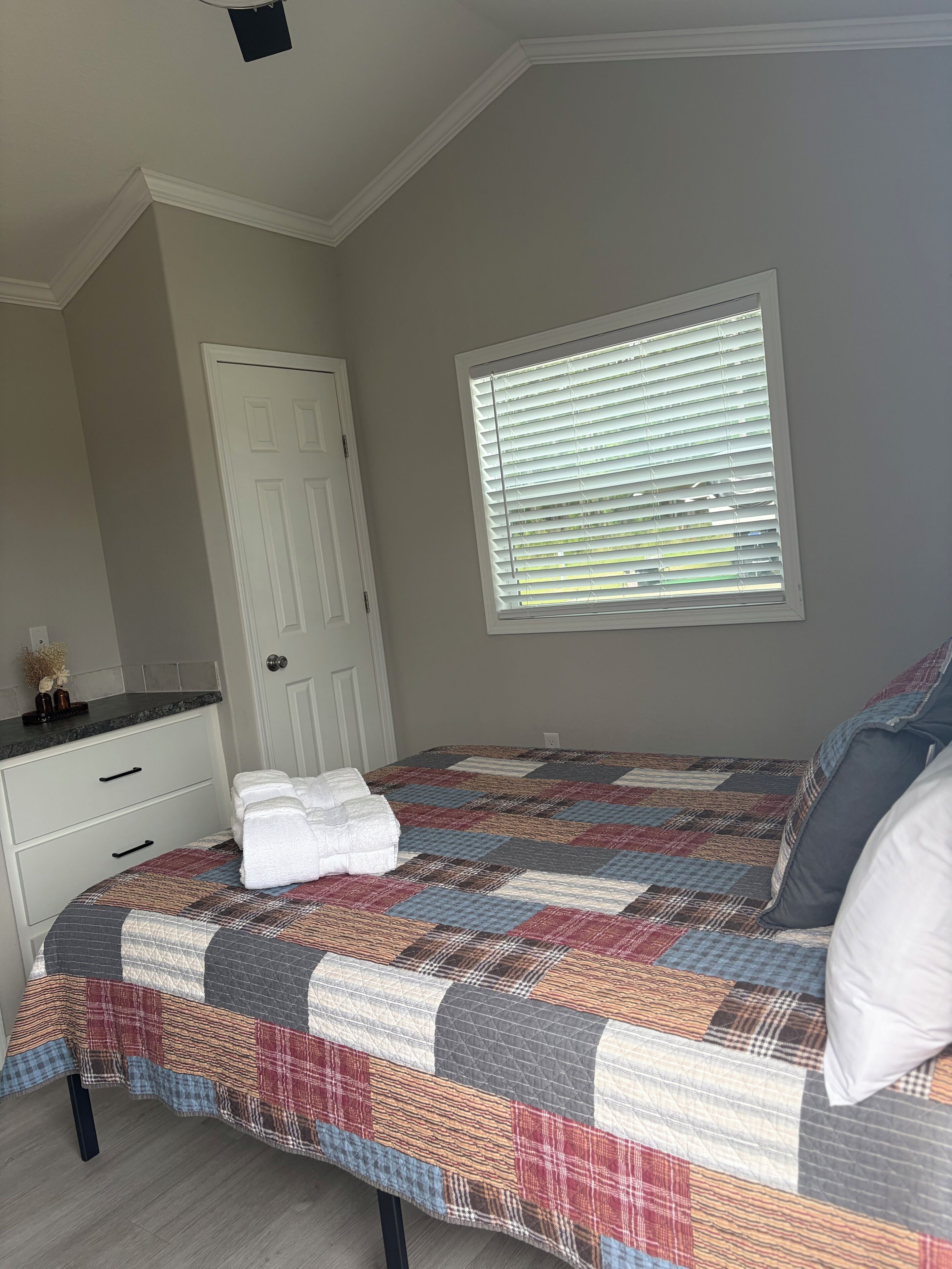 Un dormitorio con cama, ventana con persianas, puerta y cómoda.