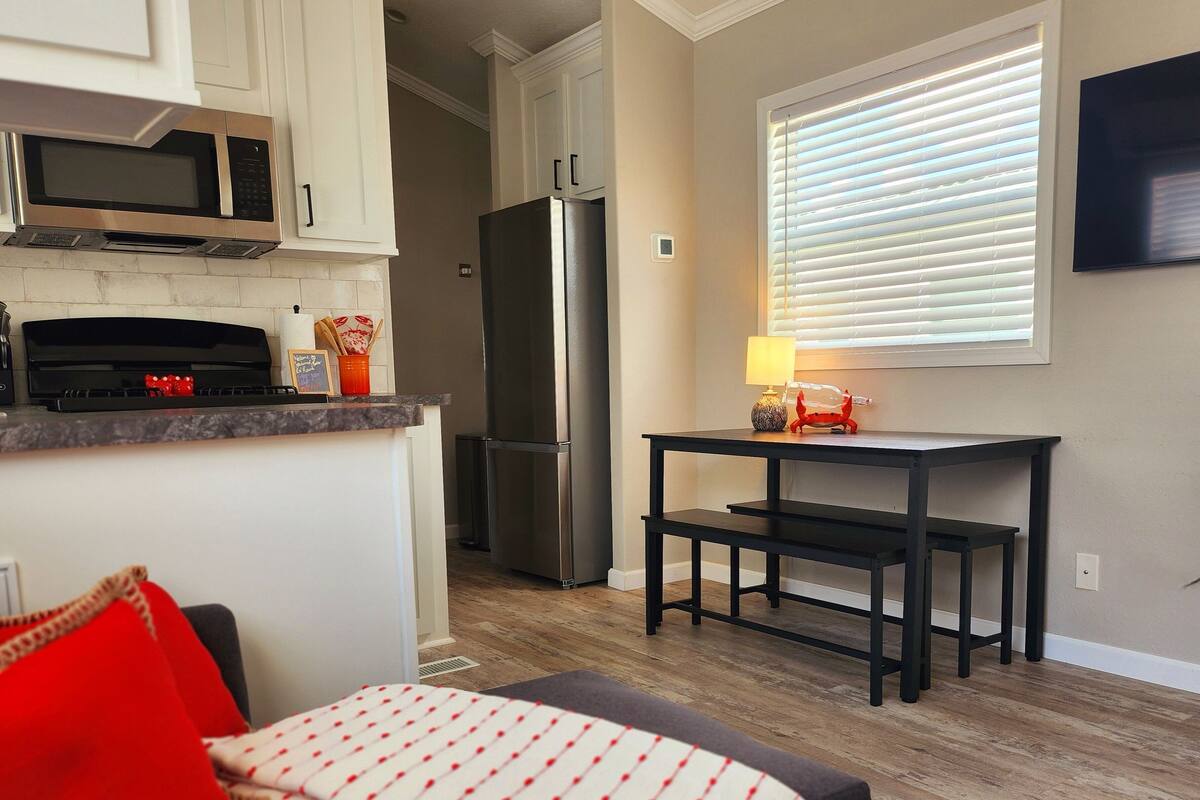 Una cocina compacta con microondas, estufa, refrigerador y un comedor con mesa y banco.