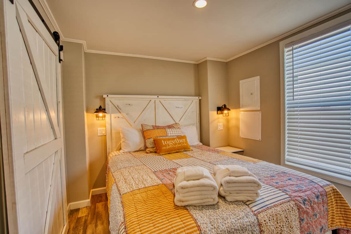Un dormitorio con cama, cabecero, lámparas de noche, ventana con persianas y puerta.