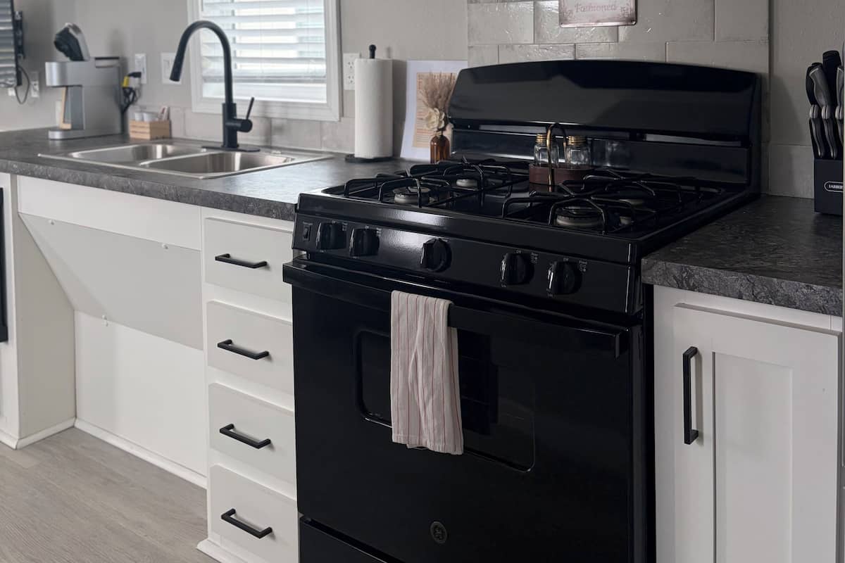 Una cocina con armarios blancos, una estufa negra y un fregadero de acero inoxidable.
