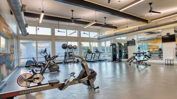 Un gimnasio con equipo de ejercicio, ventanas amplias y ventiladores de techo.