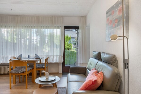 Un salon avec un canapé, une table à manger et des chaises, une lampe, et une vue à travers une porte.