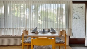 A dining table with chairs, a window with sheer curtains, and a radiator below. - Apartment 'Gertrud' with Shared Terrace and Shared Garden (Schönwald im Schwarzwald)