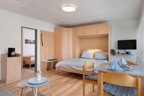 Une chambre à coucher moderne et bien éclairée, avec un lit, une table de chevet et un téléviseur fixé au mur.