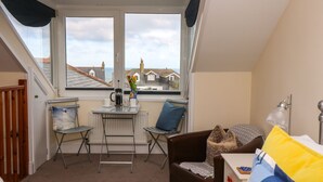 A small, cozy room with a view of the sea, a table with chairs, a bed, and a radiator. - Breakers Point (St Ives)