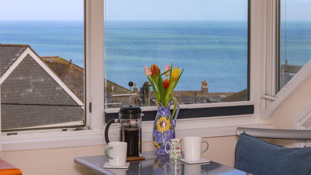 A table with a coffee maker, a vase with flowers, and two mugs by a window overlooking the sea. - Breakers Point (St Ives)