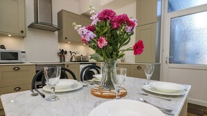 A kitchen with a marble countertop, a vase of flowers, and a dining table set for four. - Breakers Point (St Ives)