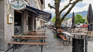 Een terras met houten tafels en banken, een bord met een Ierse pub en een berg op de achtergrond.