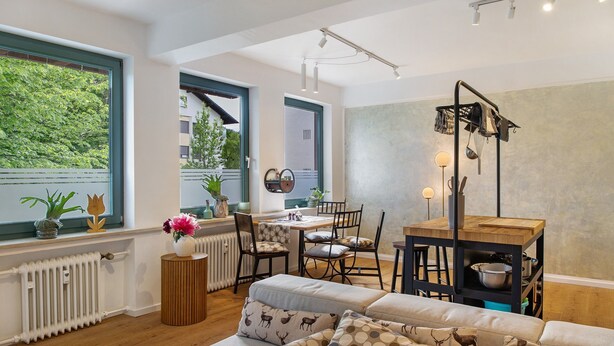 Een moderne woonkamer met een bank, eettafel, stoelen en uitzicht op groen.