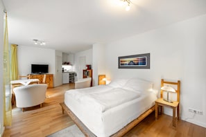 A bedroom with a bed, bedside table, lamp, and a TV in the adjacent room.