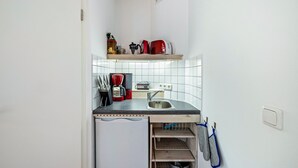 A compact kitchen with a built-in oven, a sink, and a shelf above the countertop holding a kettle and a toaster. - Studio 'Remke' with Private Terrace and Wi-Fi (Starnberg)