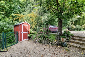 A red shed, a tree, a car, and a stone wall with steps leading up.