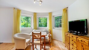 A room with a sofa, a dining table with chairs, a TV on a wooden cabinet, and windows with curtains. - Studio 'Remke' with Private Terrace and Wi-Fi (Starnberg)
