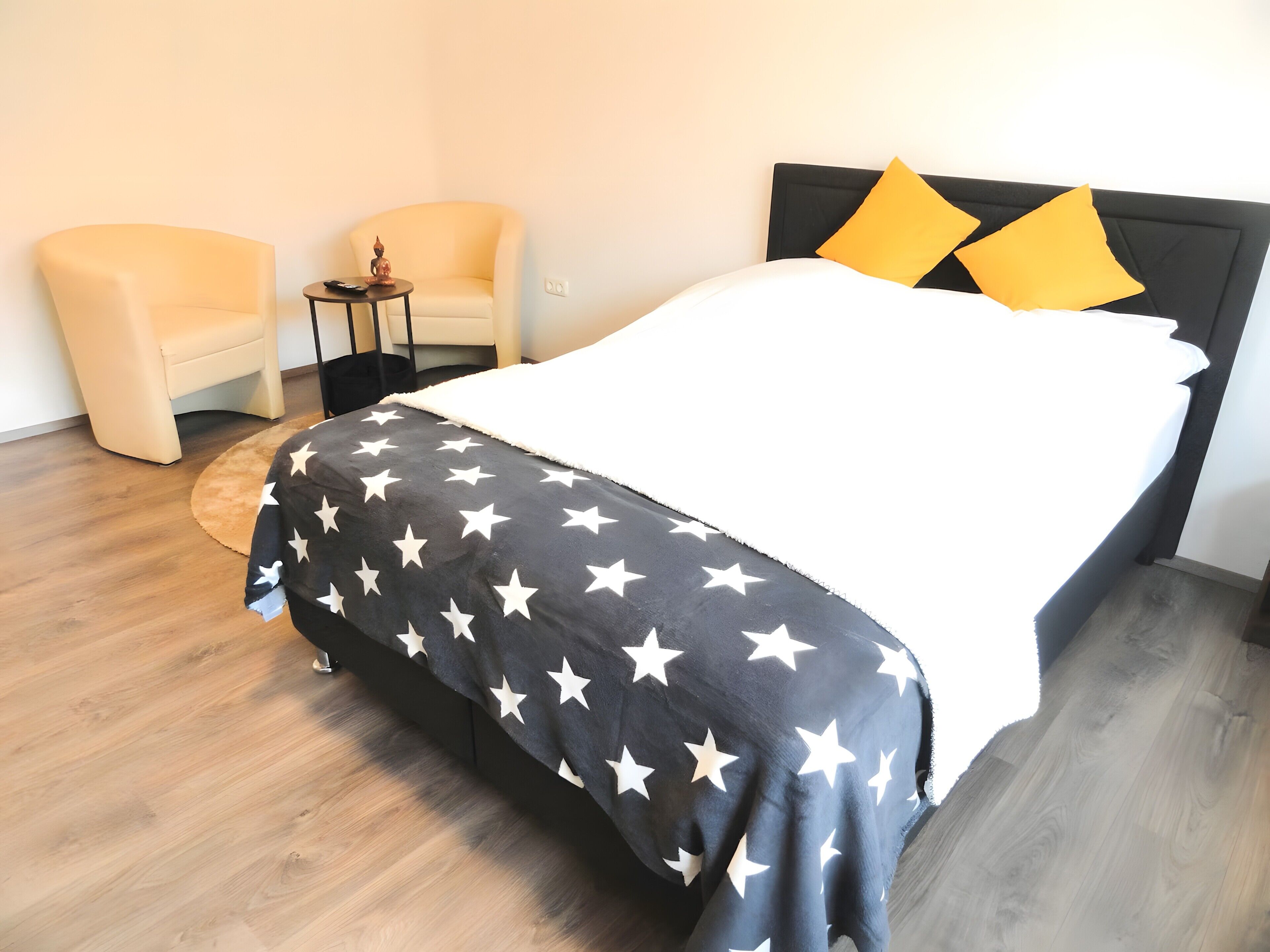 Un letto con una coperta a motivi stellati bianchi e neri, due cuscini gialli e una testiera nera.