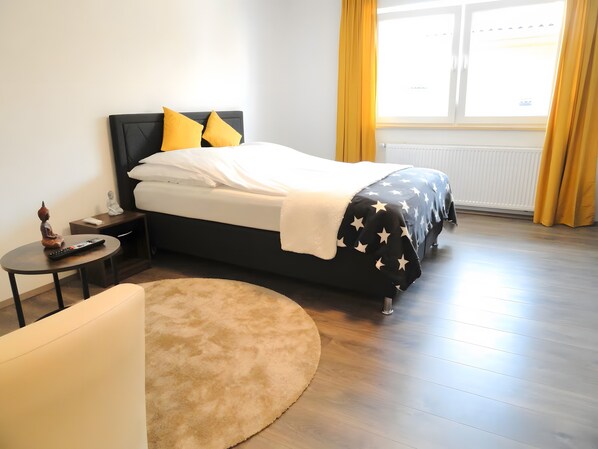 A bedroom with a bed, bedside table, and a small table with a remote control. - Apartment 'Karins Pension Room 4' with Wi-Fi (Lampertheim)