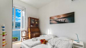 A bedroom with a bed, a nightstand, a wooden dresser, a painting, and a view of the outdoors. - Mica Aurea Morcote - Villa With Terrace (Morcote)
