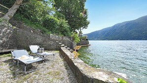 A lakeside terrace with lounge chairs, a stone wall, and a view of the lake and mountains. - Mica Aurea Morcote - Villa With Terrace (Morcote)