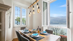 A dining area with a wooden table set for four, a view of a lake, and a window with a view of trees. - Mica Aurea Morcote - Villa With Terrace (Morcote)