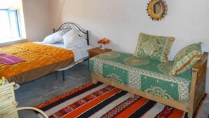 A room with two beds, one with a patterned bedspread and the other with a plain one. There is a decorative wall hanging above the bed with a green and white pattern. - Gite ditabe tafoukte  (Imi N'Oulaoune)