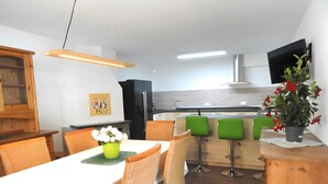 Ett modernt kök med en matplats, träskåp, en grön växt och en platt-TV.