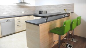 Cocina moderna con una isla central, taburetes de bar y lavavajillas.